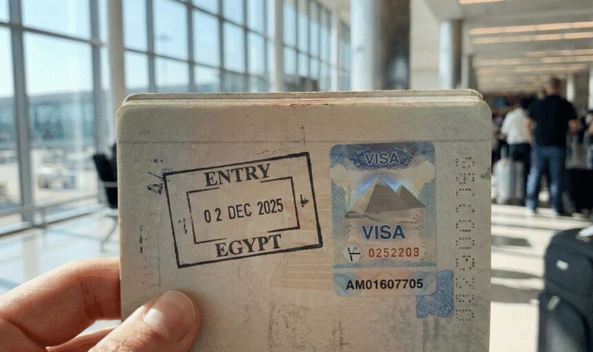 Close-up of an open passport with an Egyptian entry visa sticker and immigration stamp, held by a traveler in an airport.