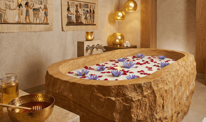 A luxurious stone bathtub filled with milk, rose petals, and lotus flowers, representing the ancient Egyptian Cleopatra beauty ritual in a spa setting.