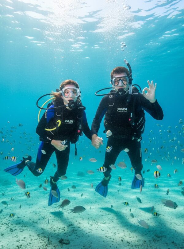 A beginner diver holding hands with an instructor during their first underwater experience.